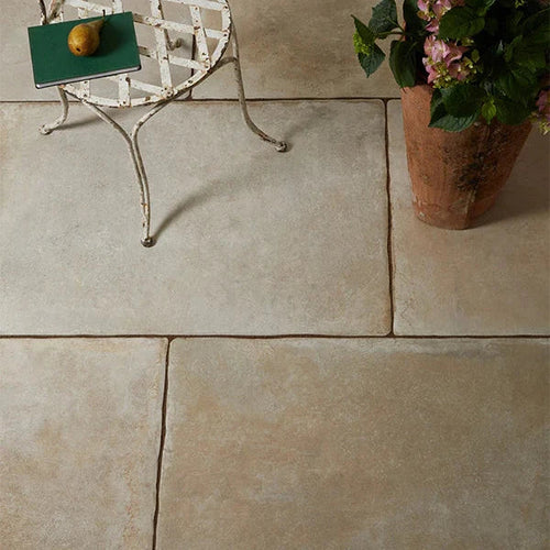Rustic stone-effect floor tiles in warm beige tones shown with a vintage metal chair and terracotta planter.