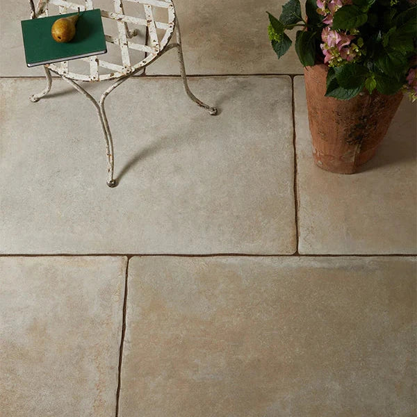 Rustic stone-effect floor tiles in warm beige tones shown with a vintage metal chair and terracotta planter.