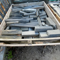 Stack of wooden planks on a pallet against a stone wall.