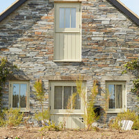 Stone house with beige window frames and greenery