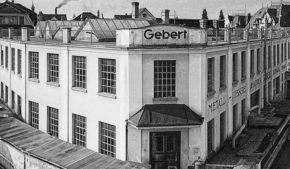 Historical black and white photograph of a building with 'Gebert' branding on the roof.