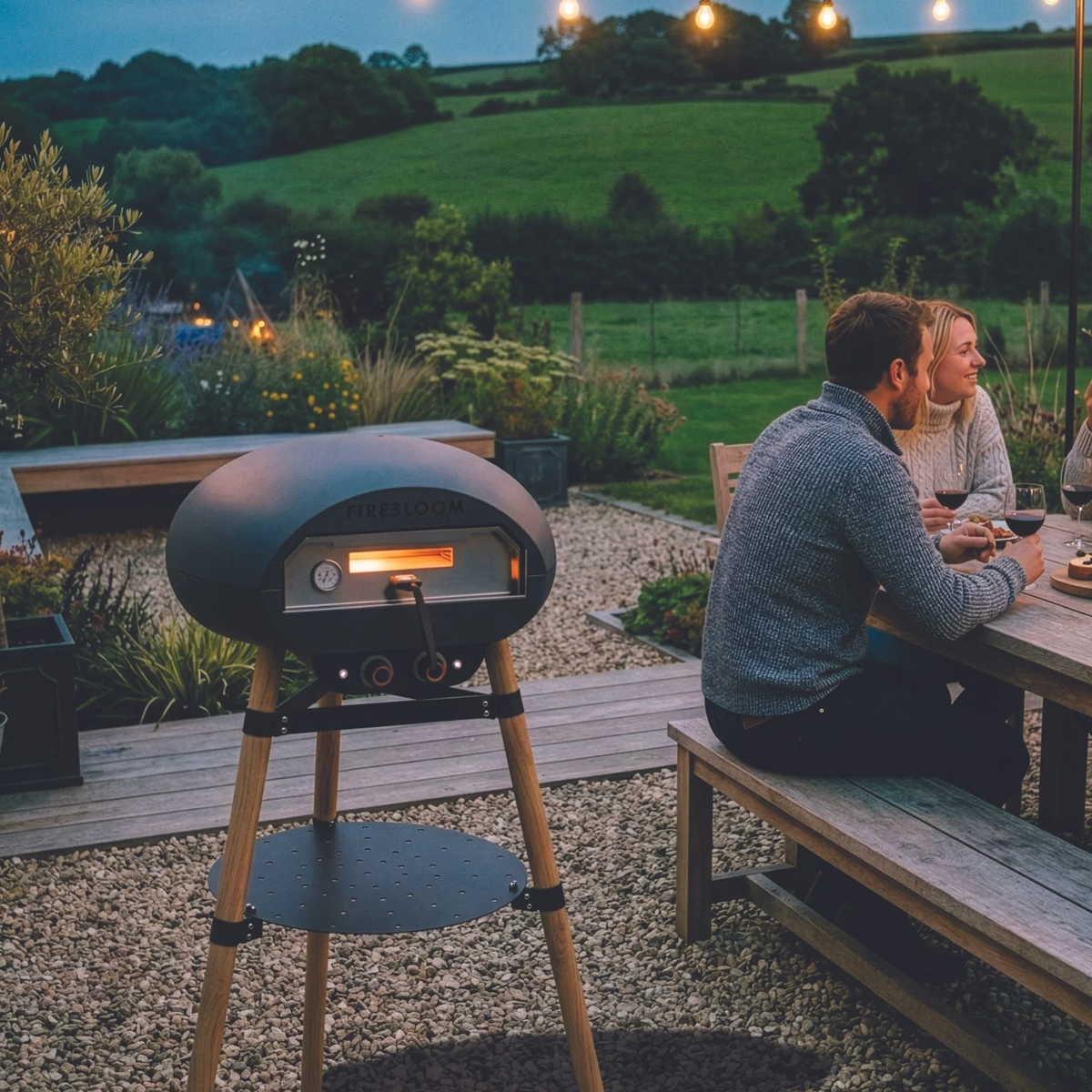 People sitting at a table with an outdoor pizza oven in a garden setting.