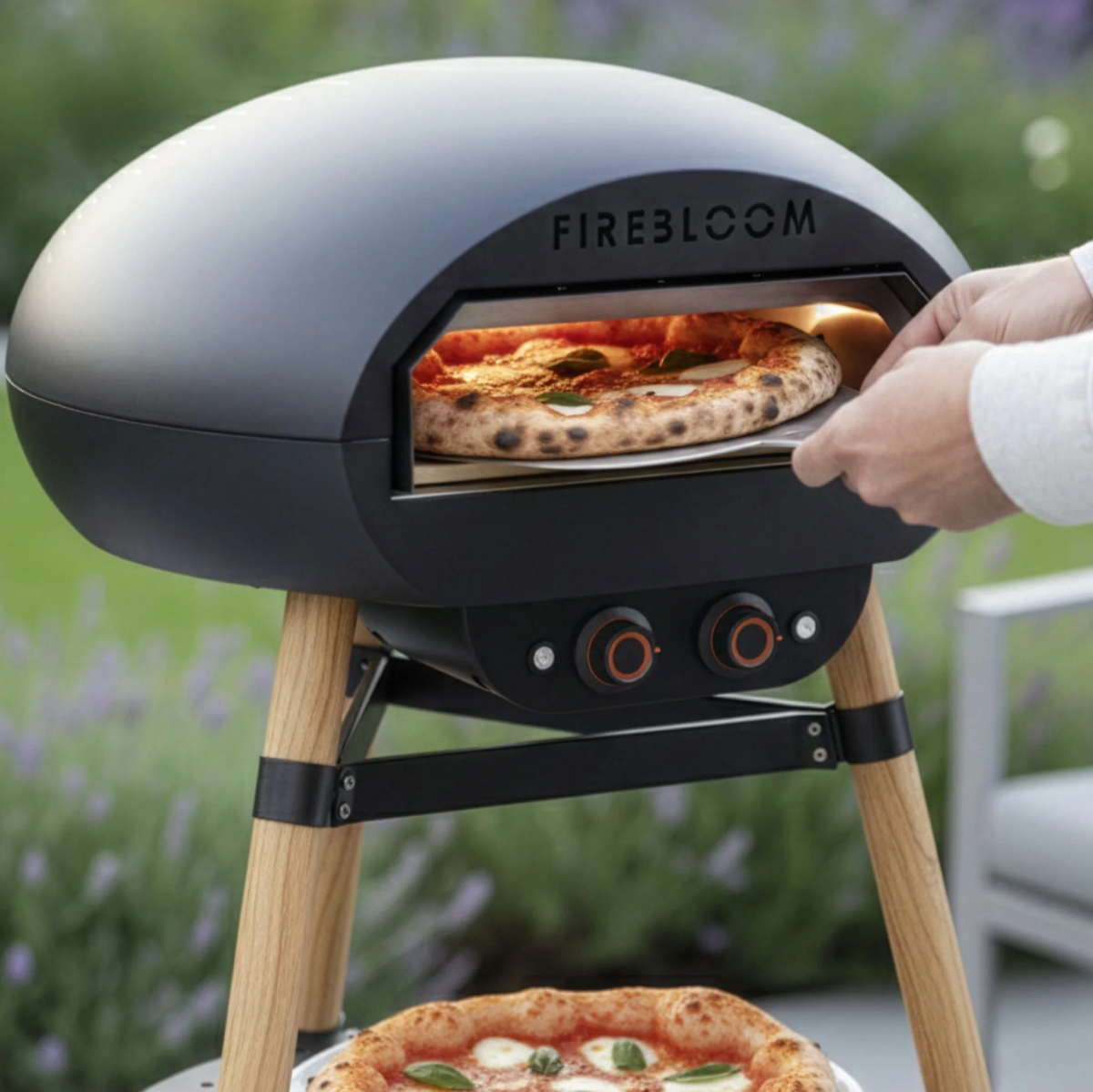 Portable pizza oven with a pizza being cooked outdoors, featuring the brand 'Firebloom'.