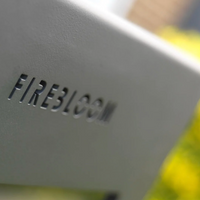 Close-up of a product with 'FIREBLOOM' branding against a blurred natural background.