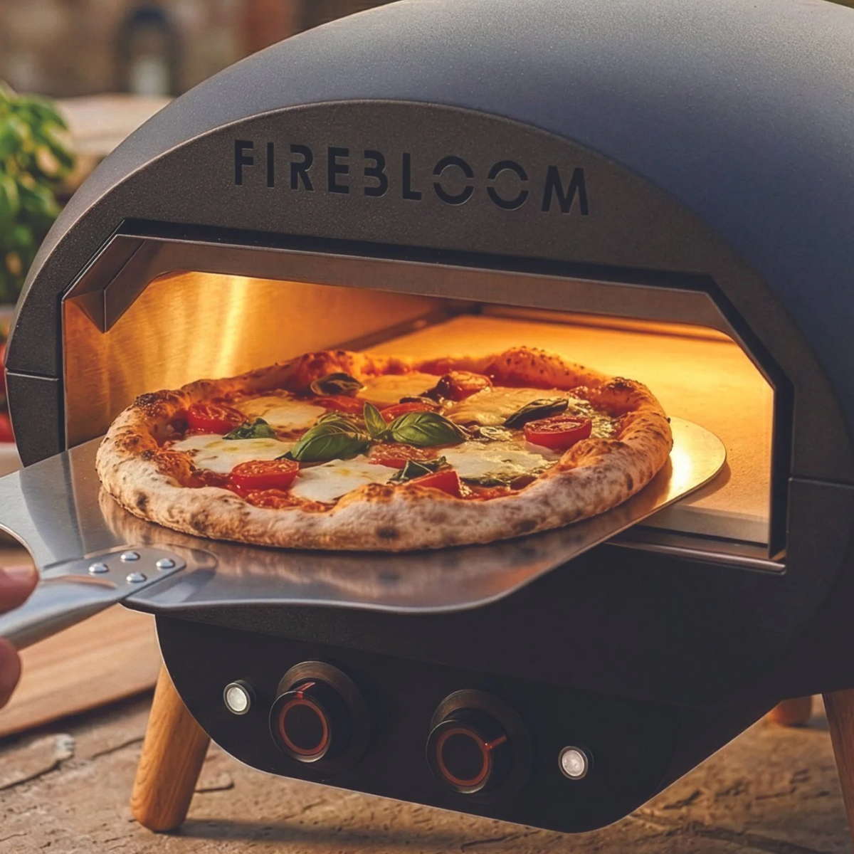 Firebloom pizza oven with a pizza inside, on a wooden surface.