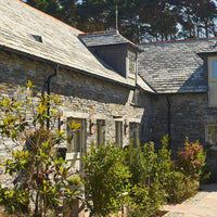 Stone building with a sloped roof and windows, surrounded by greenery.