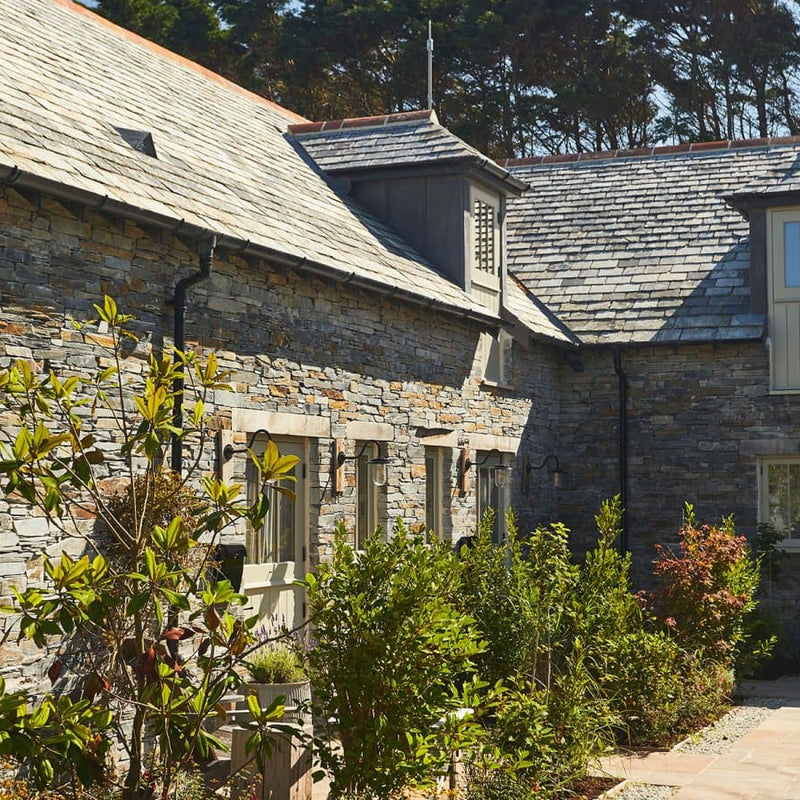 Stone building with a sloped roof and windows, surrounded by greenery.